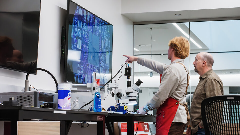 A student and faculty discuss a circuit board in the Electronics Shop.