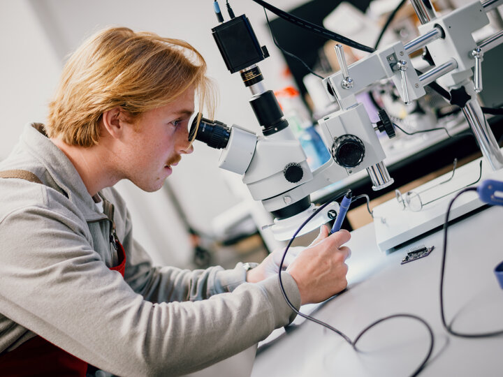 A student inspects a circuitboard under a microscope.